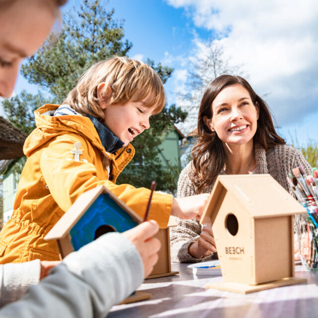Zwei Kinder und eine Frau beim Basteln eines Vogelhaus