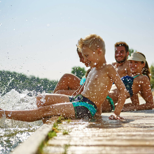 Eine Familie sitzt auf einem Steg am See